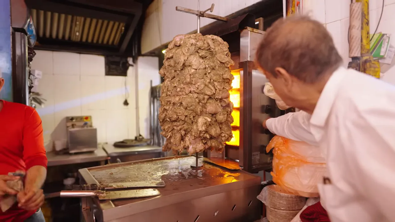 giant vertical shawarma spit with glowing vertical burners and a flat top griddle at Al‑Bake in Delhi