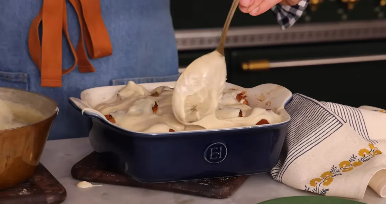 Spoon pouring vanilla custard over bread pudding in a blue baking dish