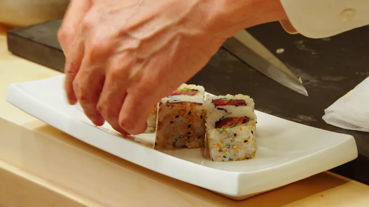 Chef's hands arranging freshly sliced inside-out spicy tuna rolls on a white rectangular plate