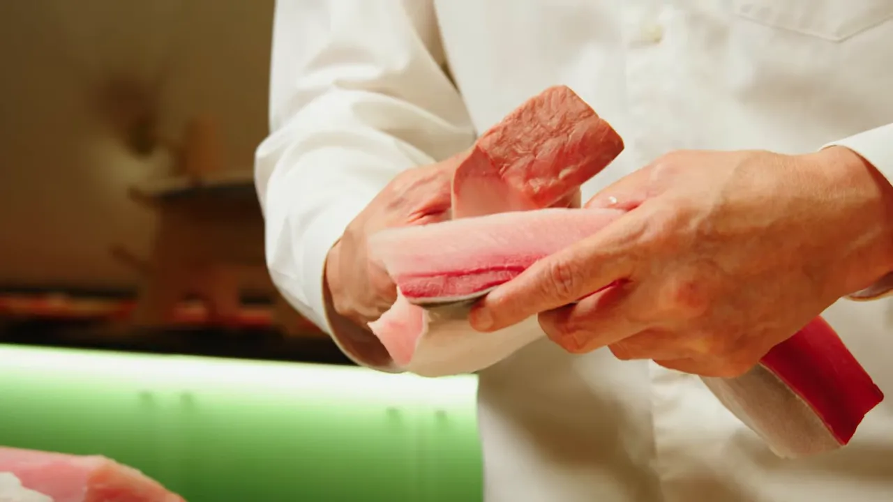 Chef's hands holding thin slices of yellowtail over a fillet, ready for use in sushi rolls
