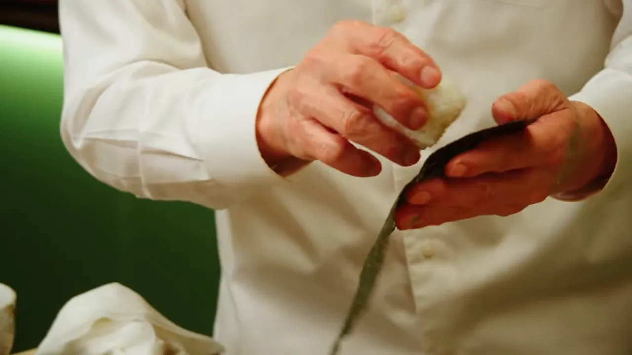 Hands placing sushi rice onto a nori sheet to form the base of a temaki hand roll