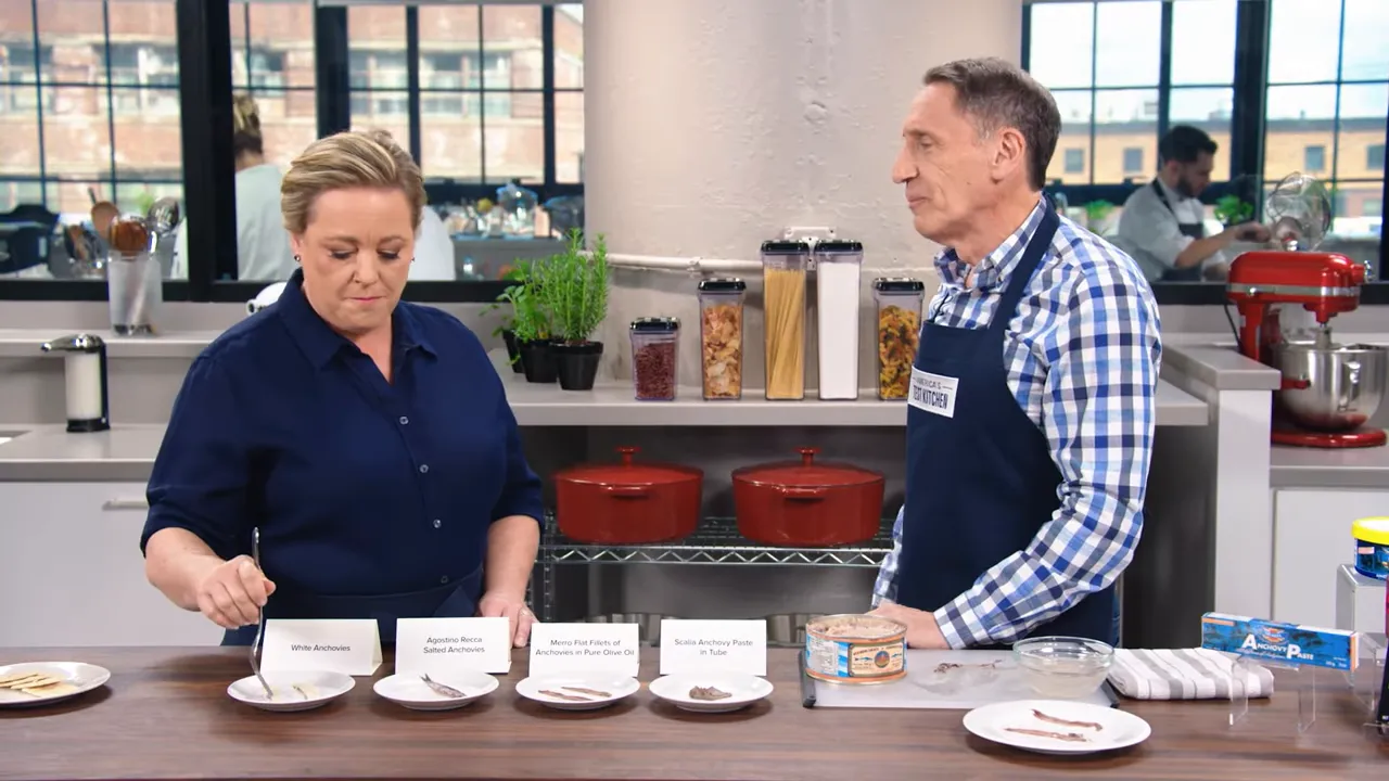 Countertop tasting lineup with labelled plates of different tinned anchovies and two presenters in the background