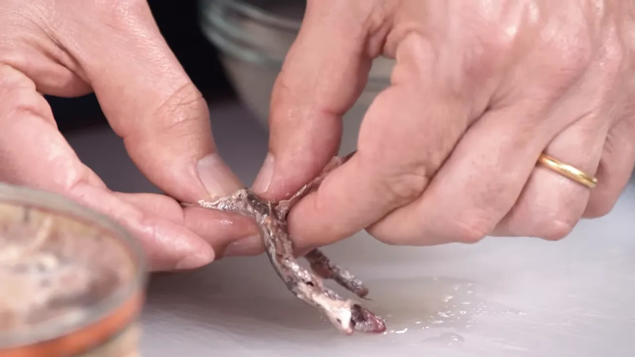 Close-up of hands deboning an anchovy fillet by separating the layers and removing the bone