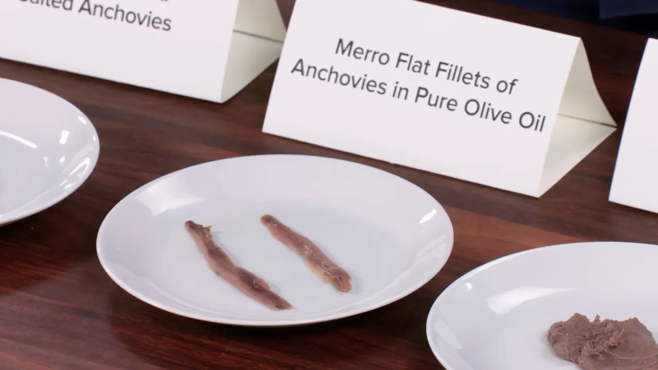 Two anchovy fillets on a white plate with anchovy paste visible on another plate and a label in the background