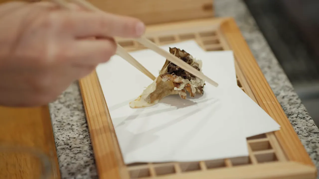 chopsticks placing a piece of tempura on paper-lined wooden tray