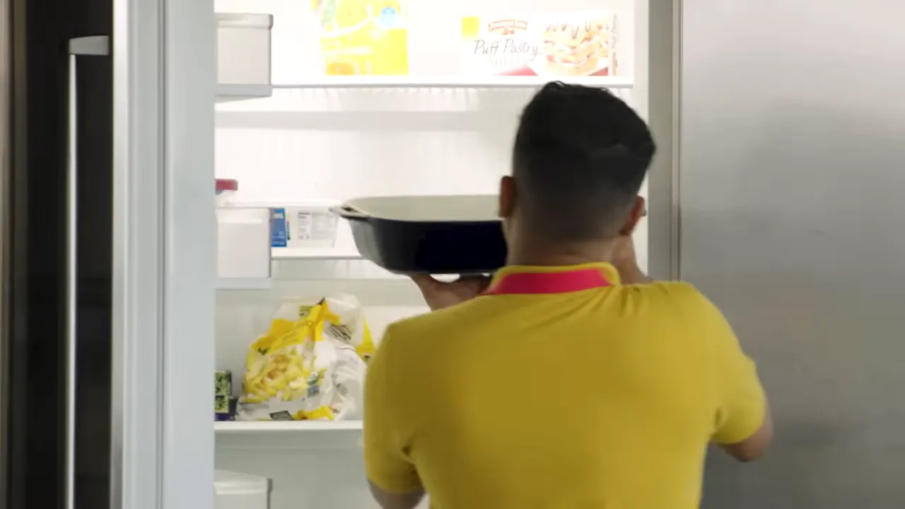 Cook from behind lifting a baking dish into an open freezer
