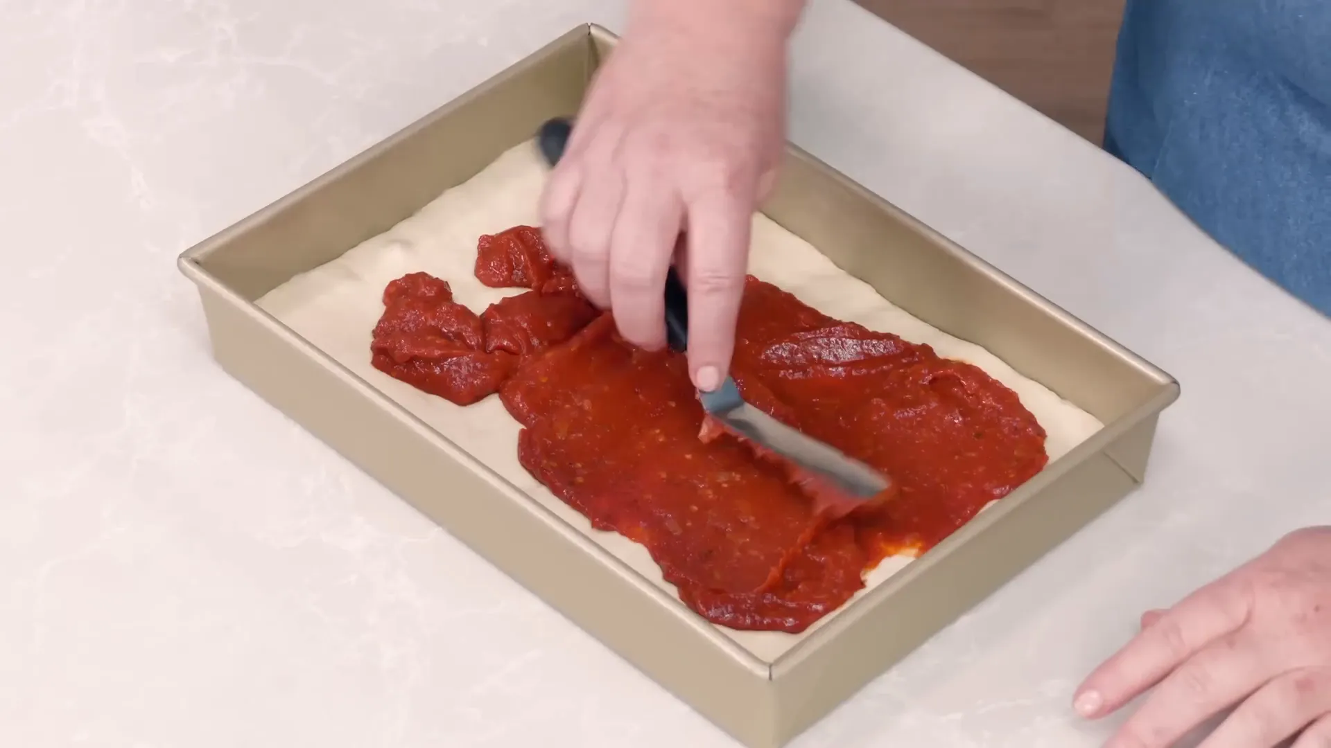 Spreading tomato sauce evenly over risen dough