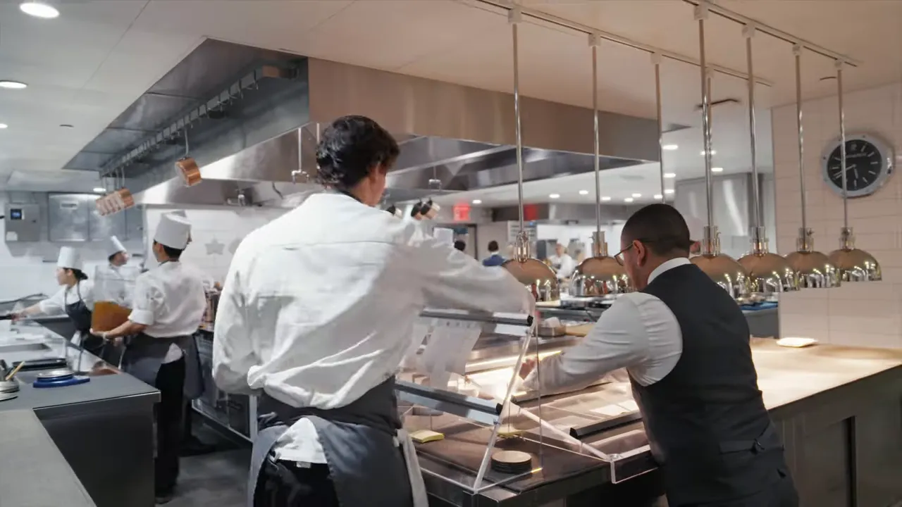 Expeditor and cooks working the pass under heat lamps in a busy kitchen