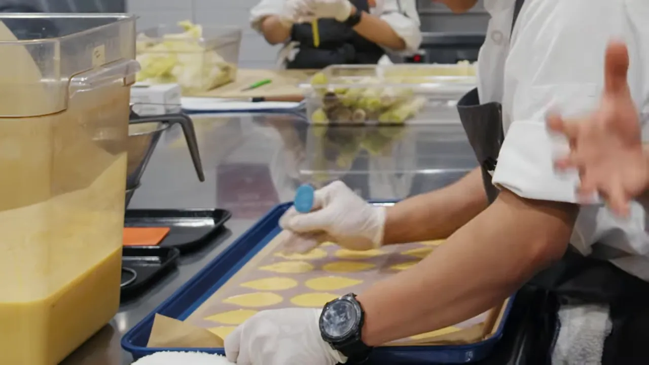 Cook wearing gloves portioning yellow sunflower-butter mixture into round molds on a tray with a container of mixture nearby.