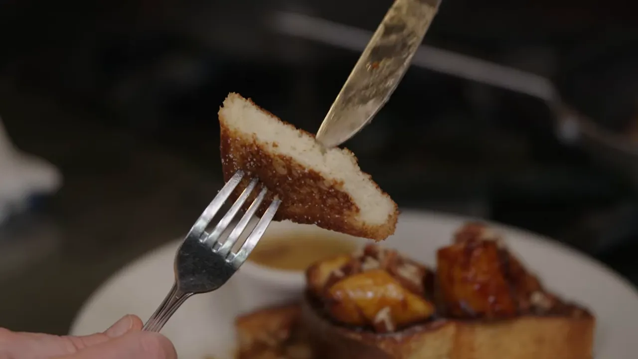 Close-up of a fork holding a small wedge of brioche French toast showing a golden seared crust and soft, custardy interior