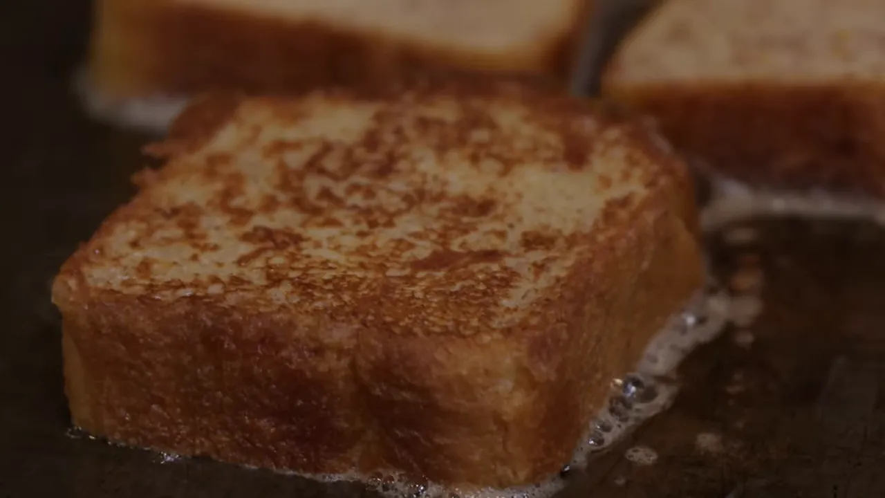 Very clear close-up of a seared brioche slice with golden, caramelized crust and butter bubbling at the edge
