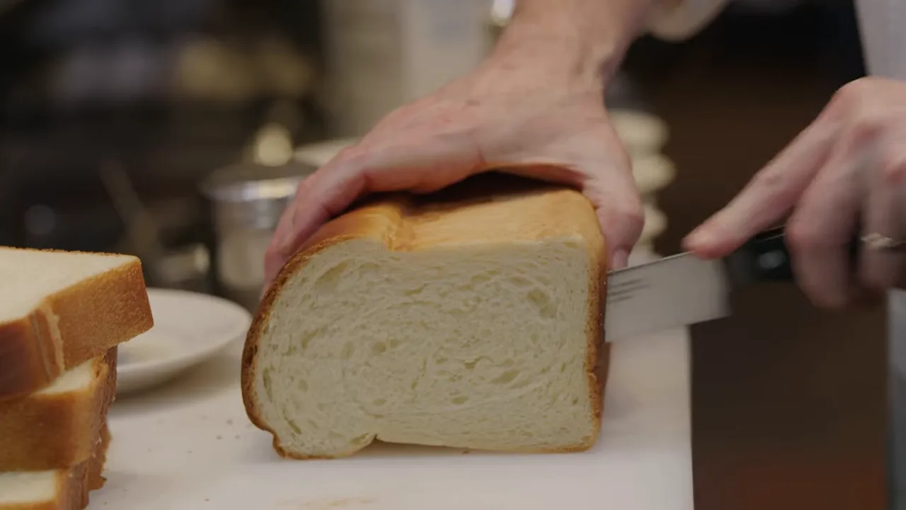 Close-up of a serrated knife cutting a brioche loaf showing the soft interior crumb