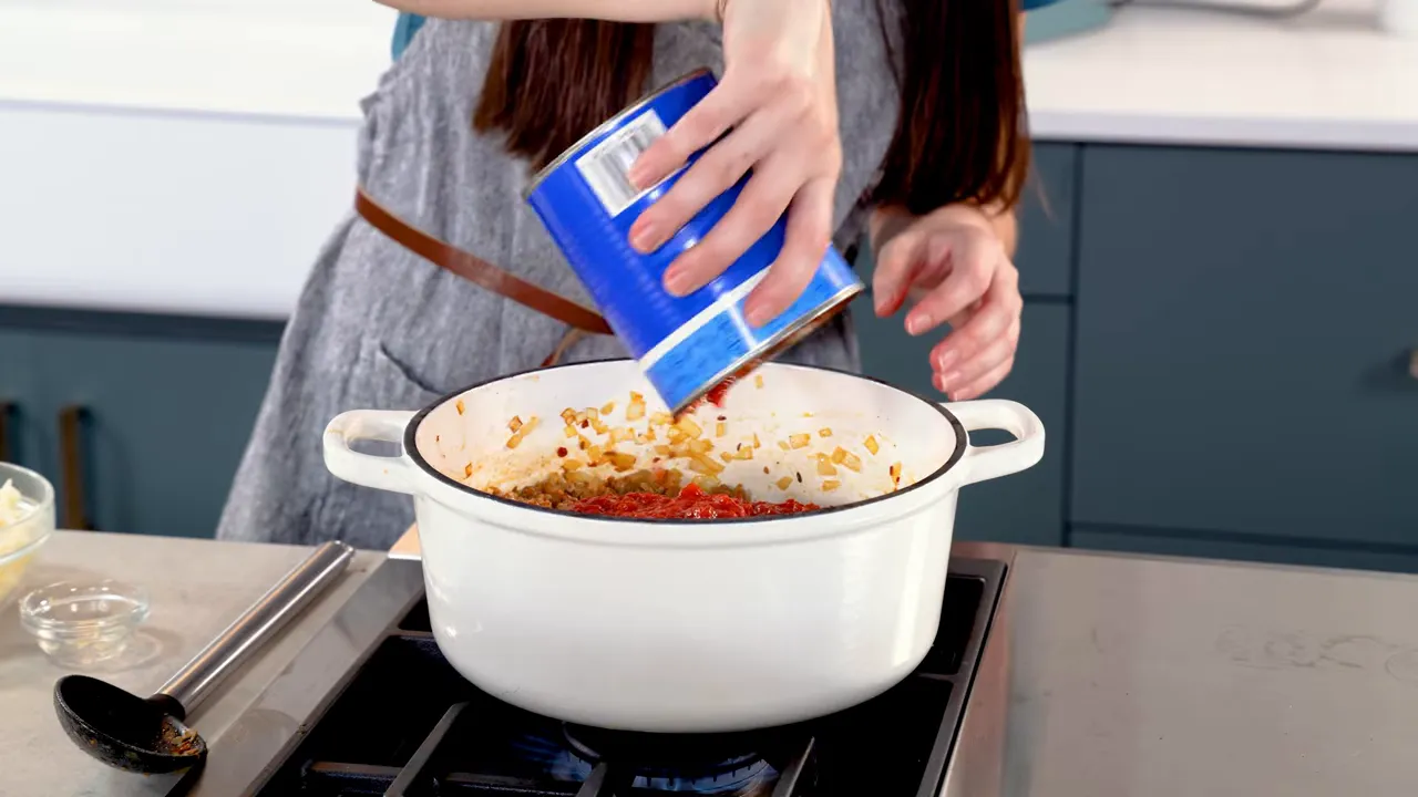 Pouring crushed tomatoes and tomato sauce into the pot