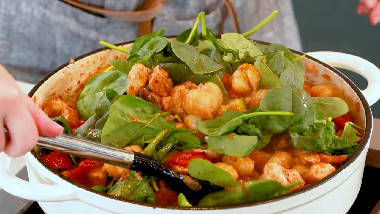 Close-up of gnocchi, browned chicken and roasted red peppers with fresh baby spinach on top in a white skillet