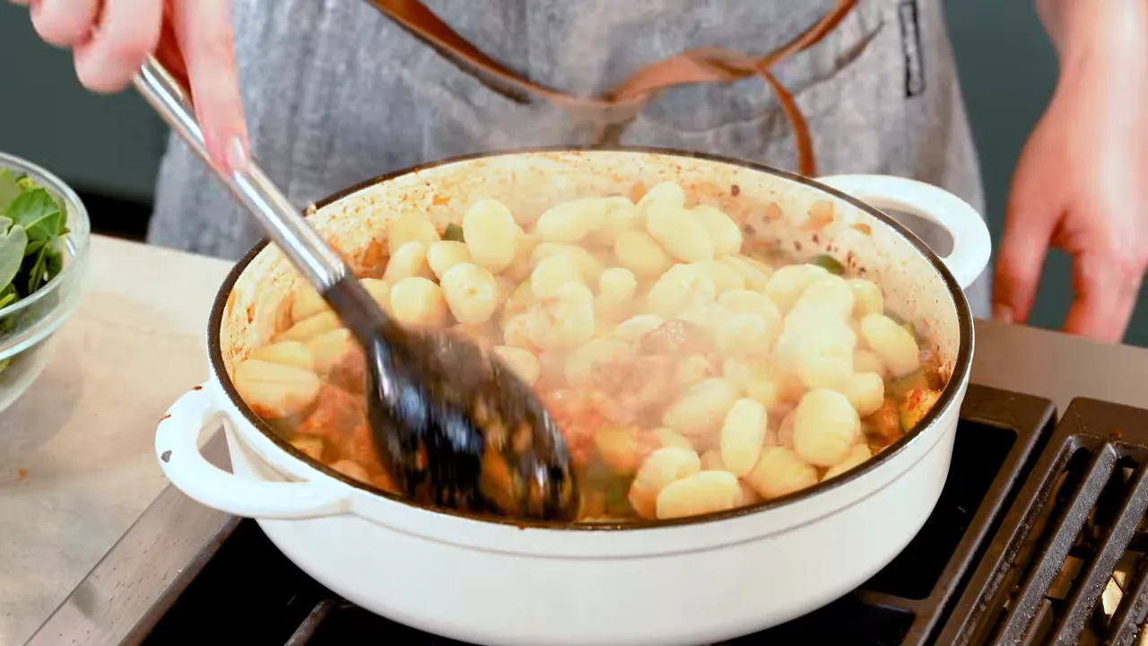 close-up of gnocchi searing in a white skillet with a black spoon and steam rising