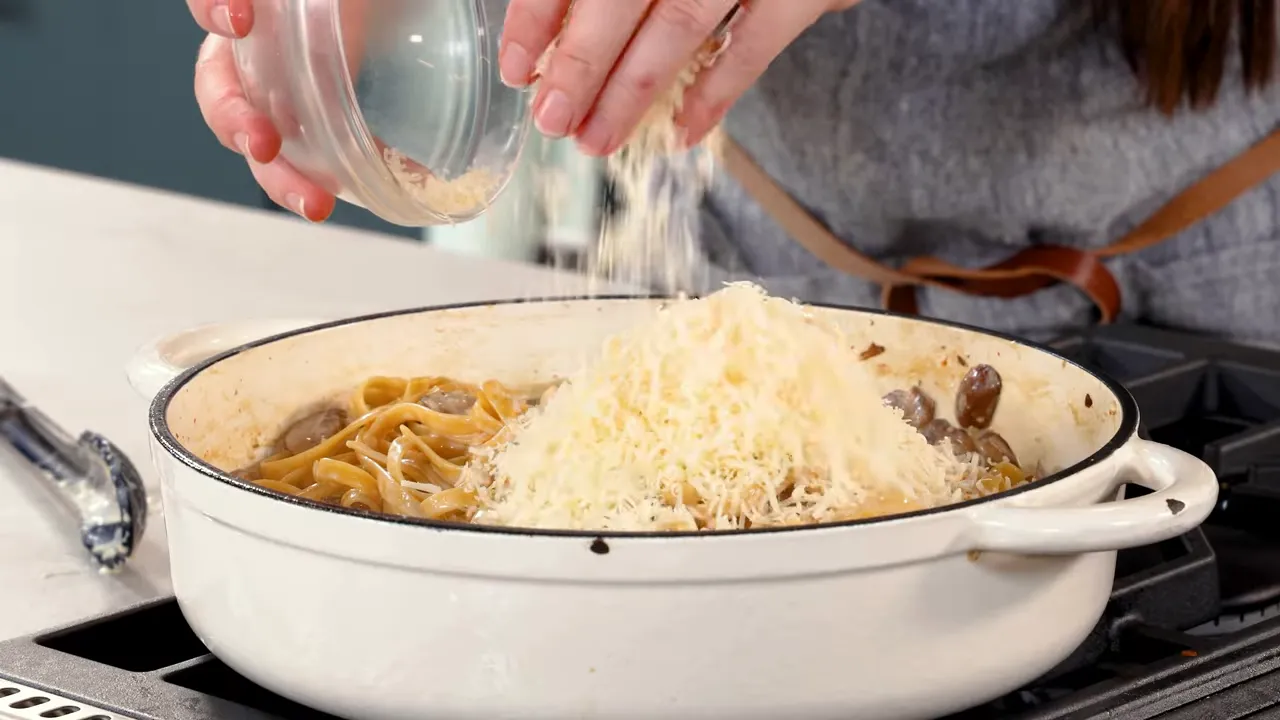 Large mound of shredded Parmesan falling into creamy mushroom pasta in skillet