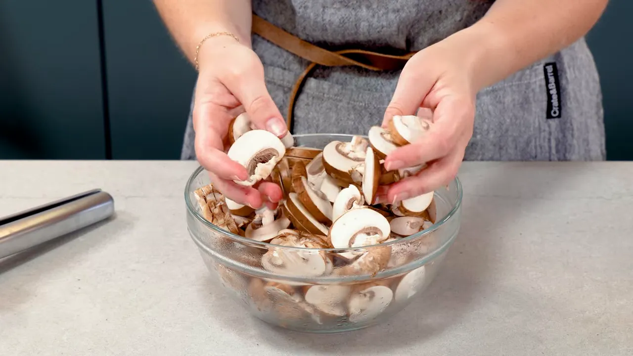close-up of hands holding and arranging sliced mushrooms in a glass bowl