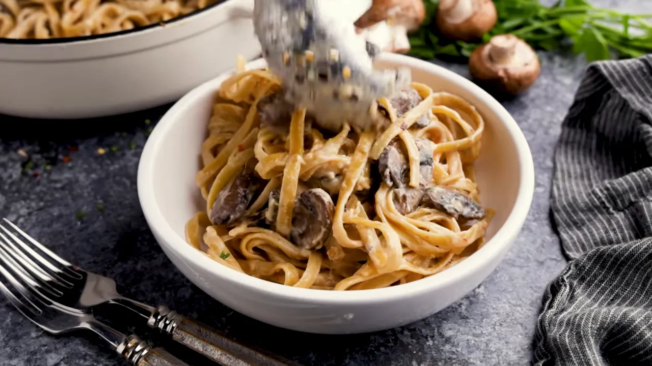 Creamy mushroom pasta being served into a bowl with tongs