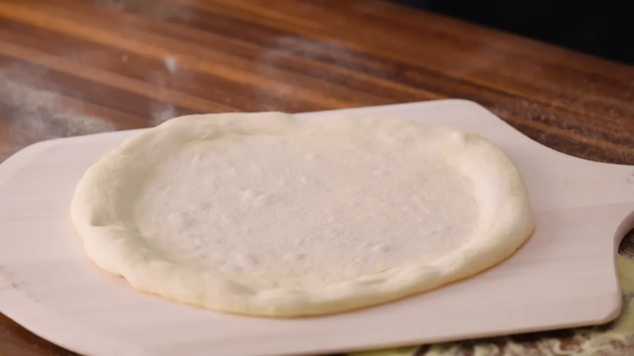 Final stretched dough on semolina-dusted peel