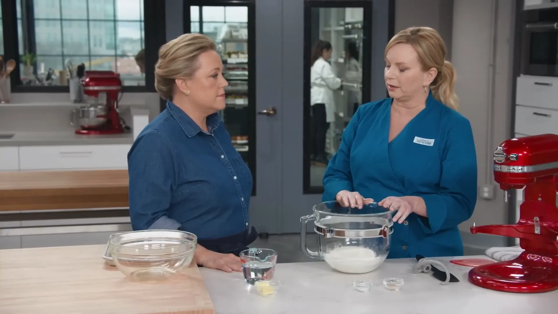 Two hosts smiling at a kitchen counter preparing pretzel dough