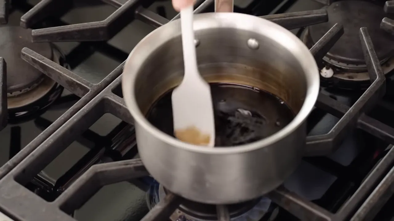 Small saucepan on a gas burner with a dark balsamic reduction being stirred with a spatula.