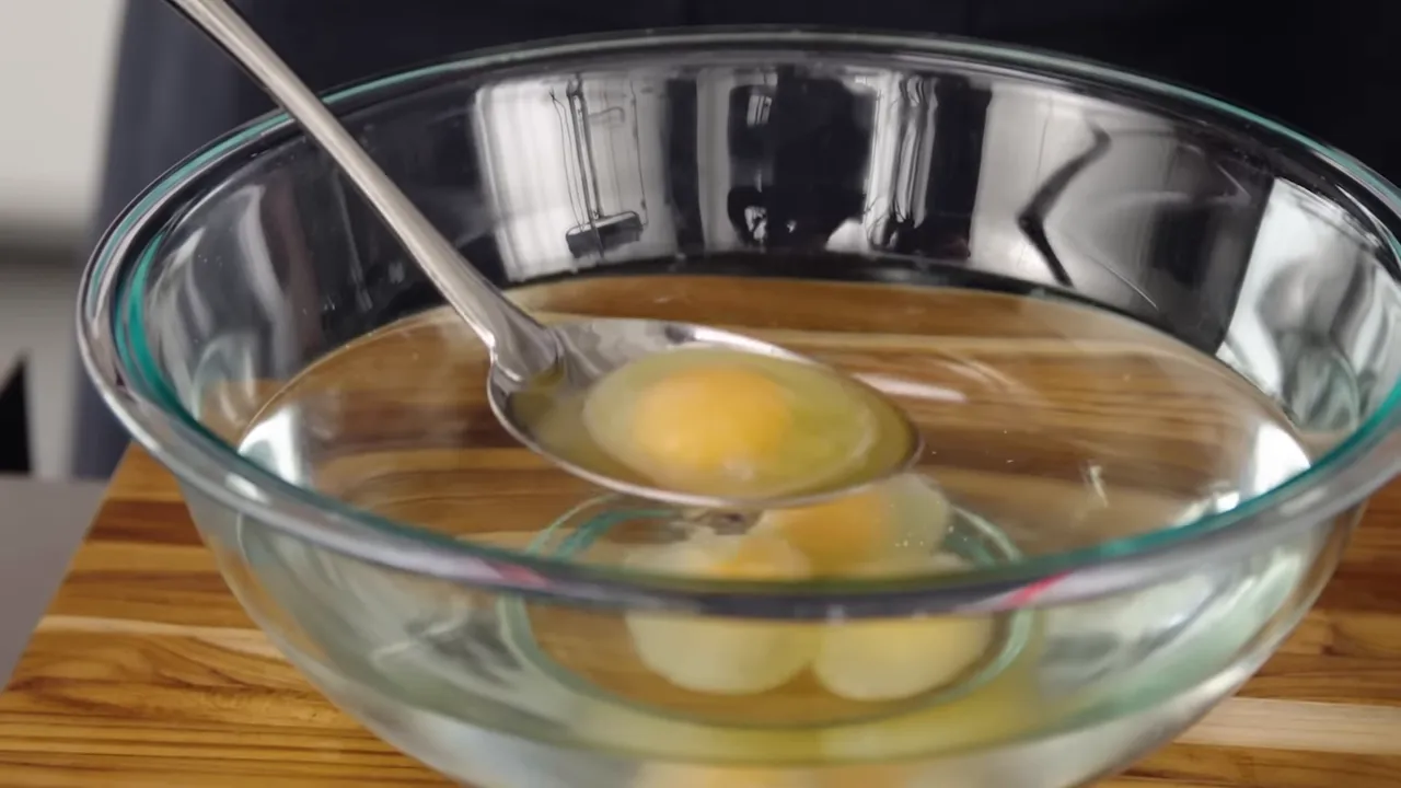 Spoon lifting an egg with opaque whites from a glass bowl, ready to poach