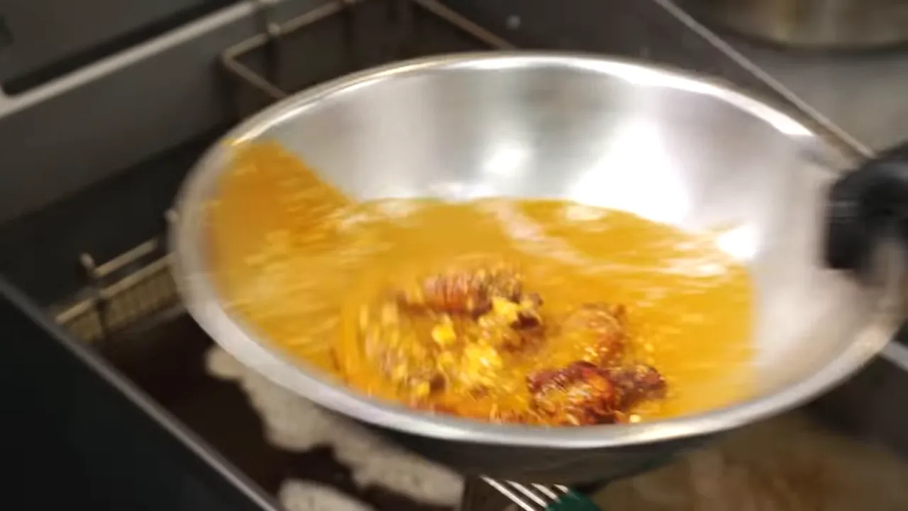 Wings being vigorously tossed in a stainless steel bowl of buffalo-style sauce over a fryer