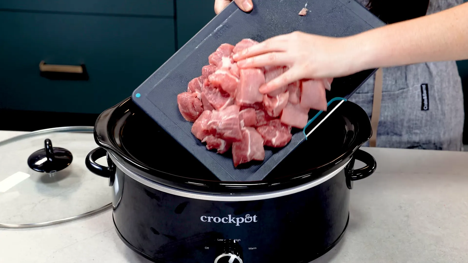 Cubed pork being added to a slow cooker