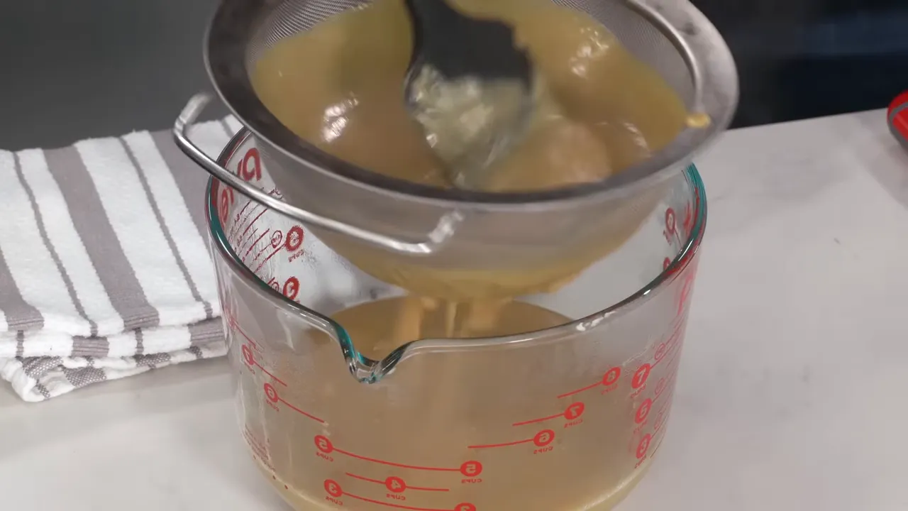 Silky, shiny thickened caramel custard draining through a fine mesh strainer