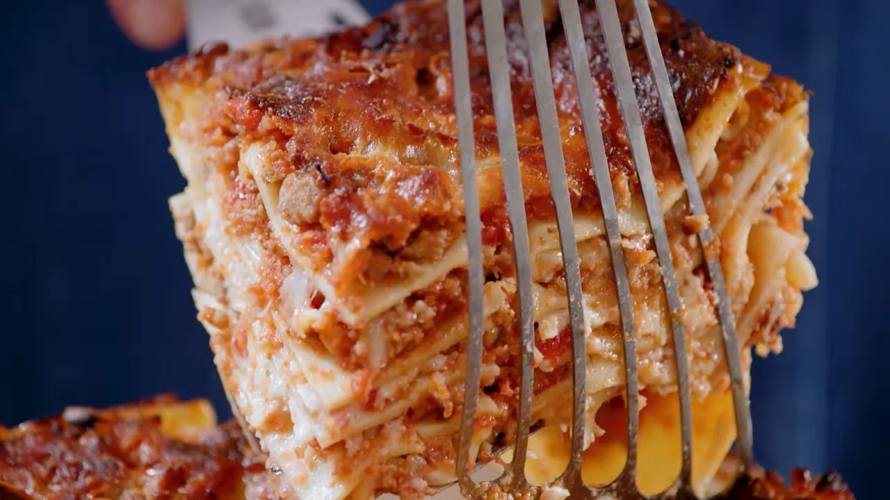 Tall slice of sausage lasagna lifted on a spatula showing neat layers and melted cheese