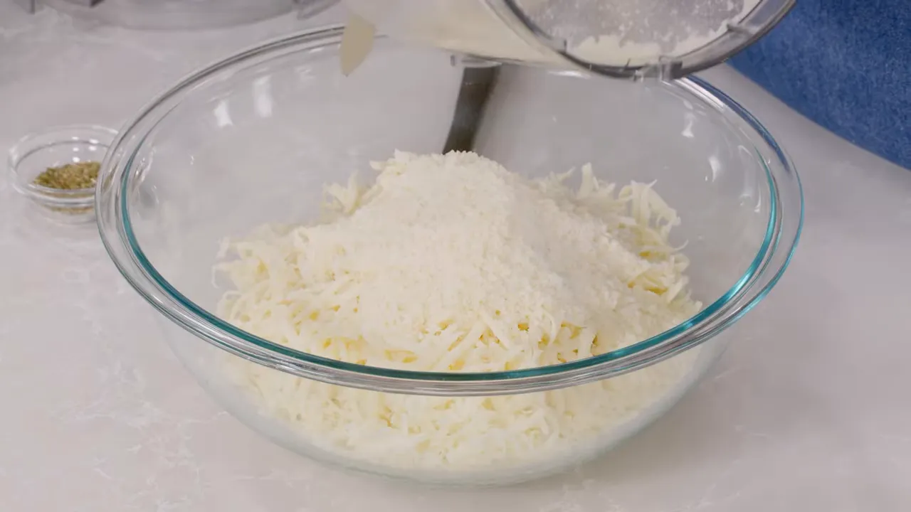 glass bowl filled with shredded mozzarella while grated Pecorino is poured in from a processor