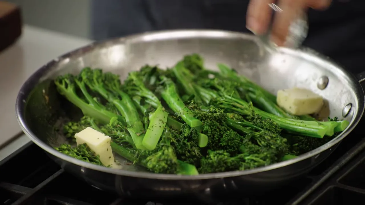 Close-up of broccolini in a stainless-steel skillet with pats of butter melting