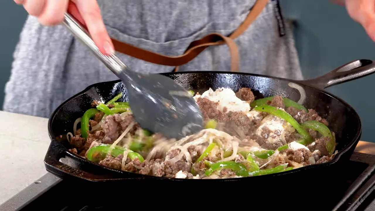 Creamy ground beef cheesesteak filling in a cast-iron skillet being stirred