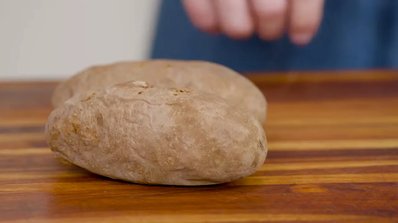 Two baked russet potatoes on a wooden cutting board with a hand approaching.