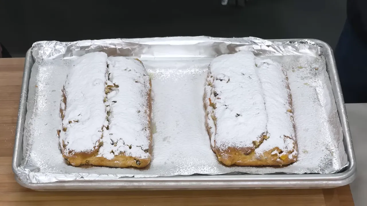 Two stollen loaves generously dusted with powdered sugar on a baking sheet