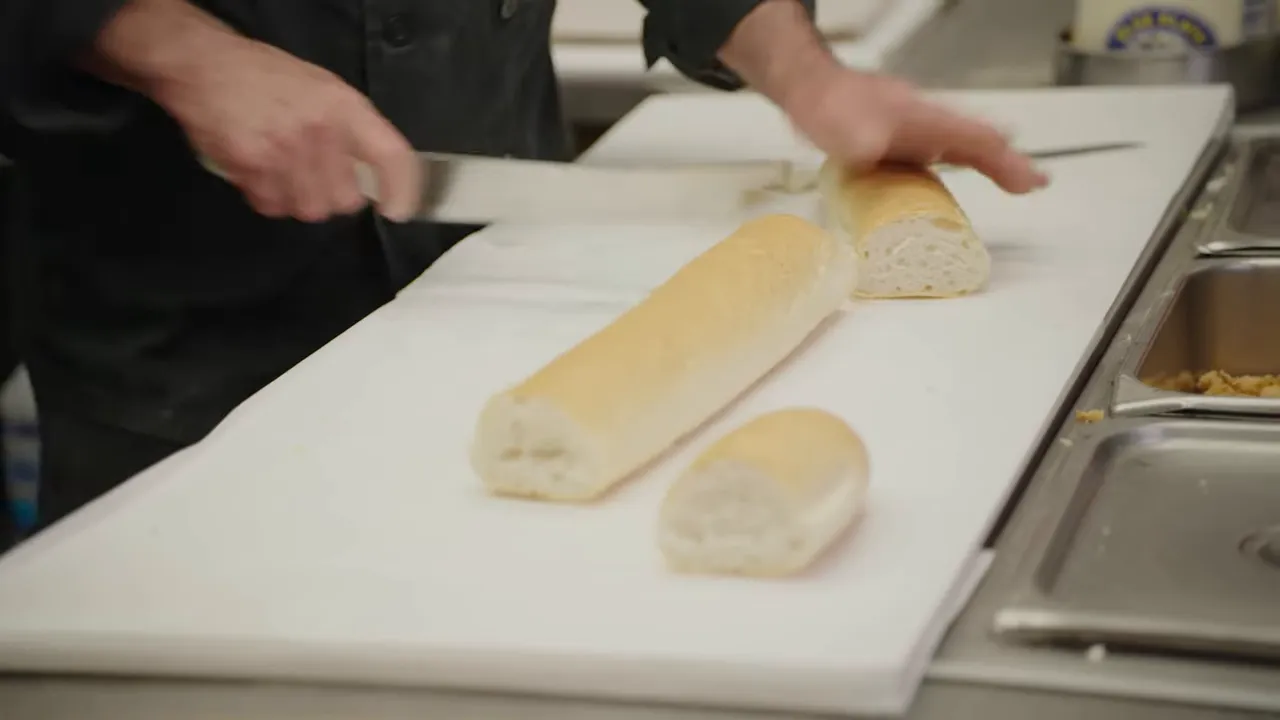 Chef slicing a same-day French loaf on a cutting board with a serrated knife