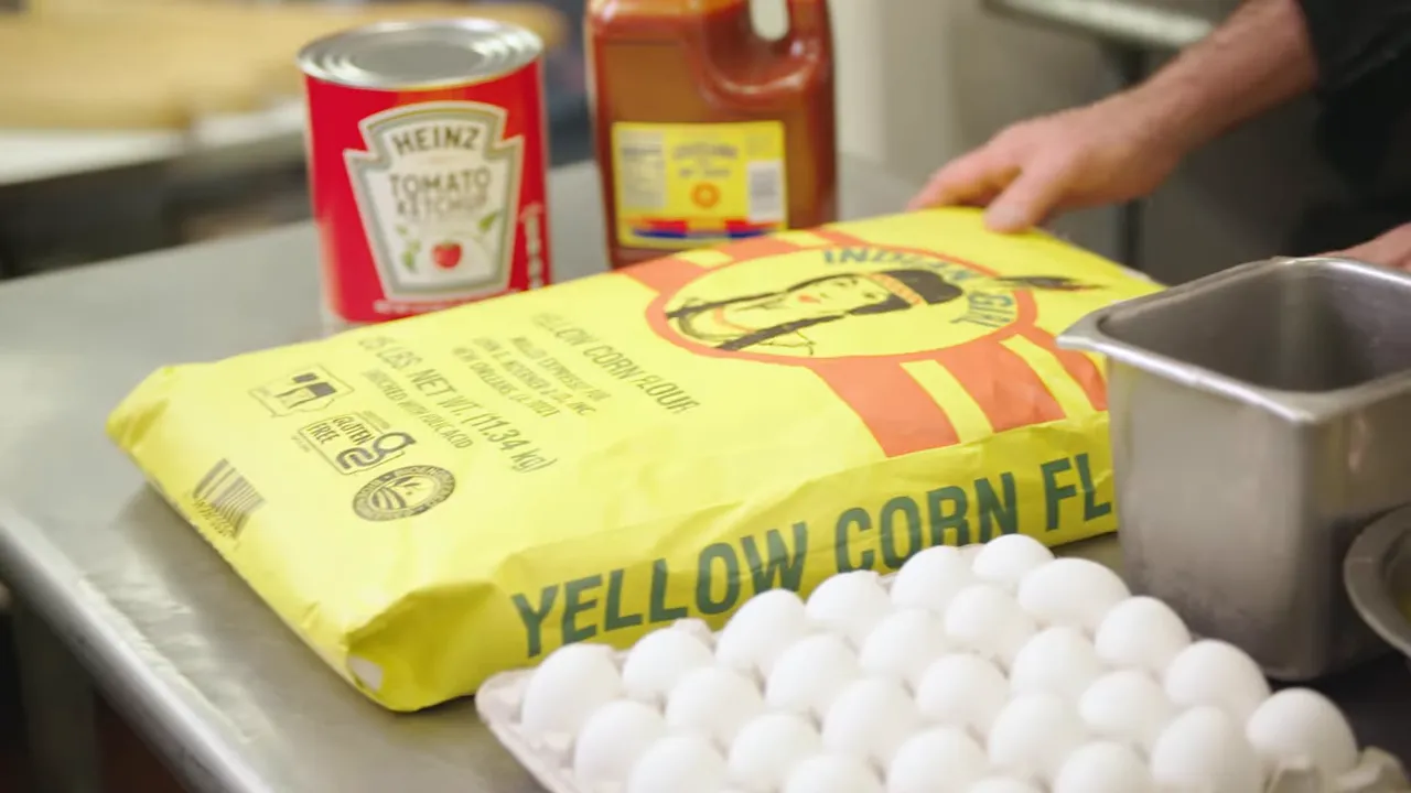 bag of yellow corn flour with carton of eggs and condiments on stainless prep table