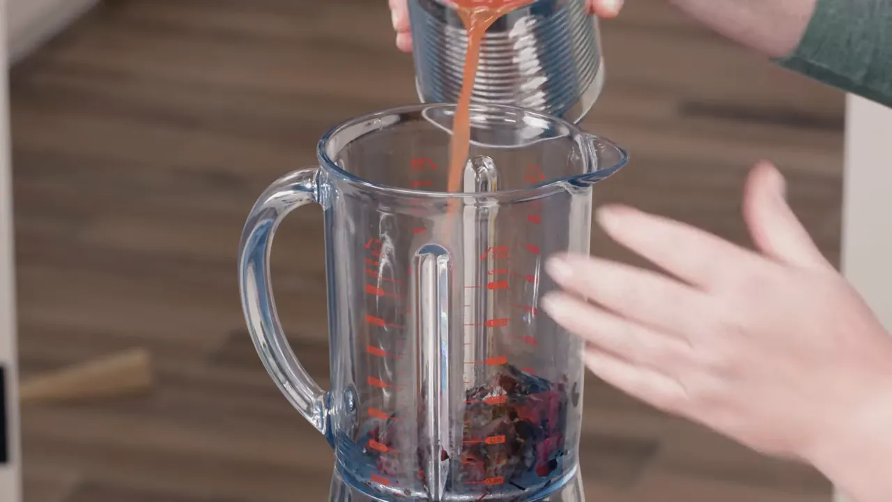 pouring canned tomatoes into a blender containing rehydrated dried chilies