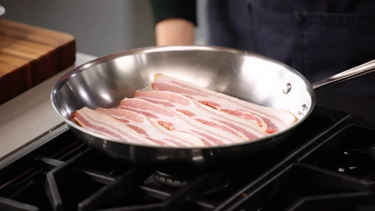 Raw bacon strips arranged flat in a stainless steel skillet ready for cooking