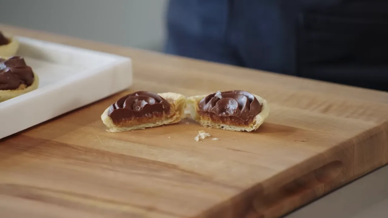 Cross-section of a mini peanut praline chocolate pie showing thin buttery crust, caramel-praline layer and chocolate namalaka on a wooden board
