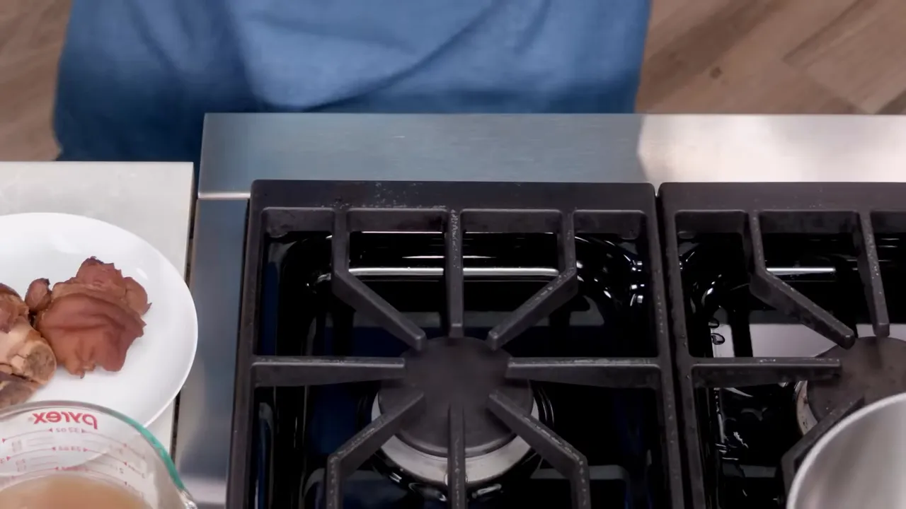 Stovetop with a plate of salt pork and a measuring cup of reserved cooking liquid beside an empty burner