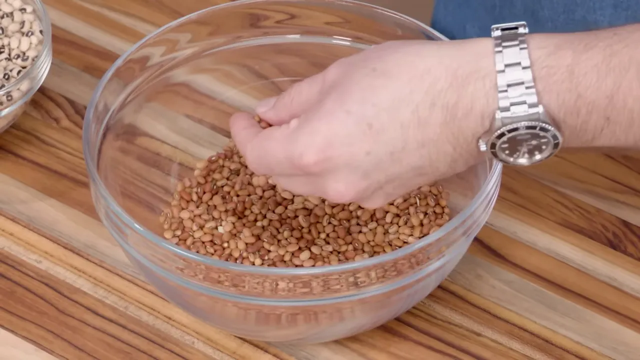 Glass bowl of Sea Island red/brown peas on a wooden cutting board being inspected by hand