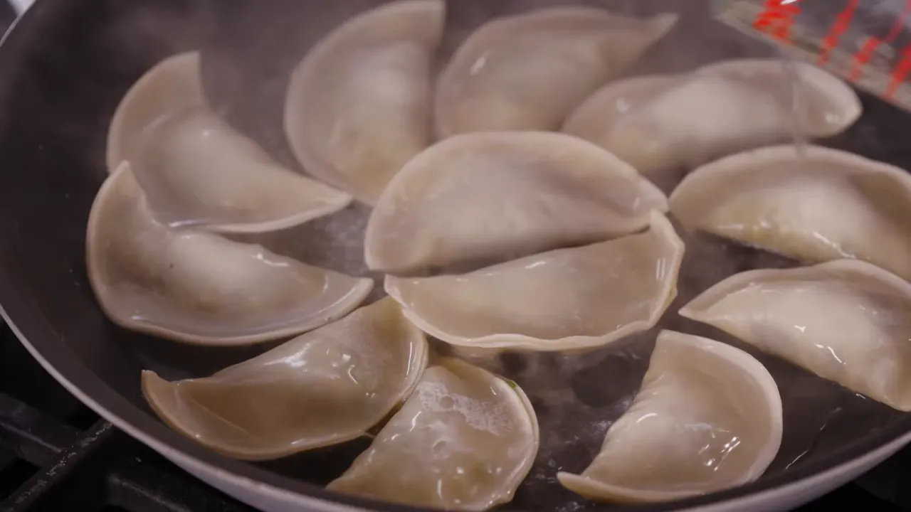 Potstickers steaming in a skillet with the wrappers starting to look translucent.