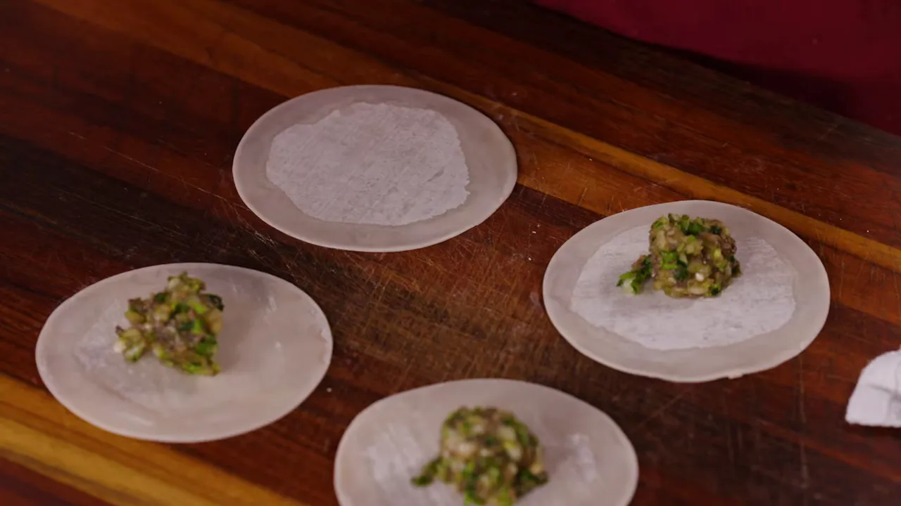 Several potsticker wrappers on a wooden board with small mounds of cabbage-mushroom filling.