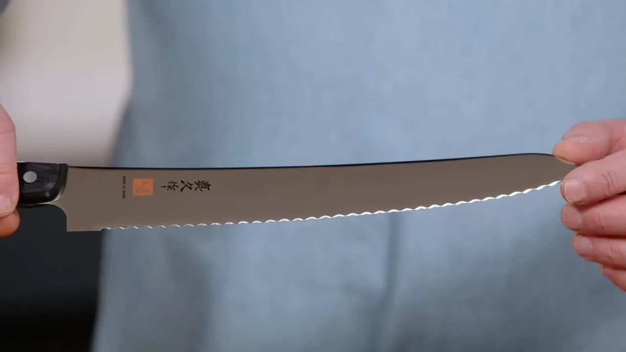 High-quality close-up of a bread knife showing pronounced triangular serrations and markings on the blade.