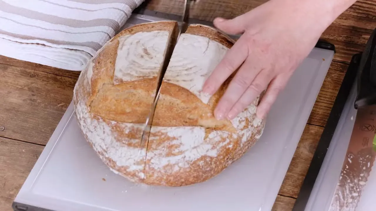 Top-down view of a serrated knife cutting a large artisan loaf, showing the length of the cut
