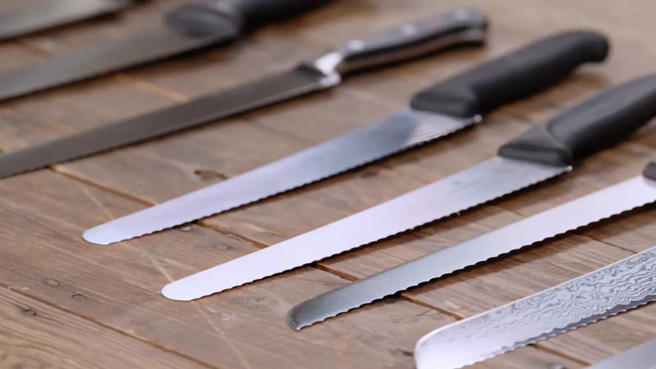 Row of serrated bread knives on a wooden table highlighting different tooth profiles and blade lengths.