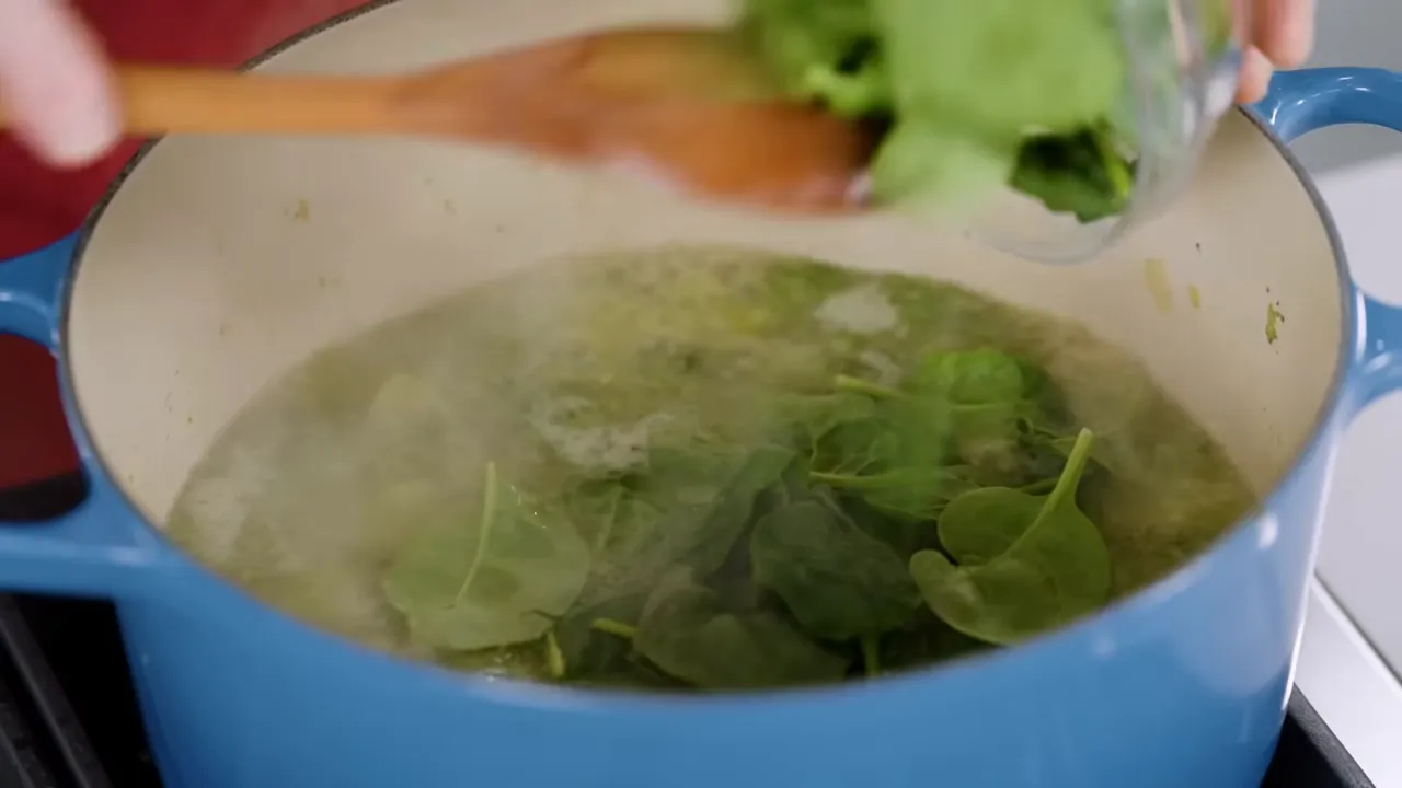 Fresh spinach being added to the pot to brighten color