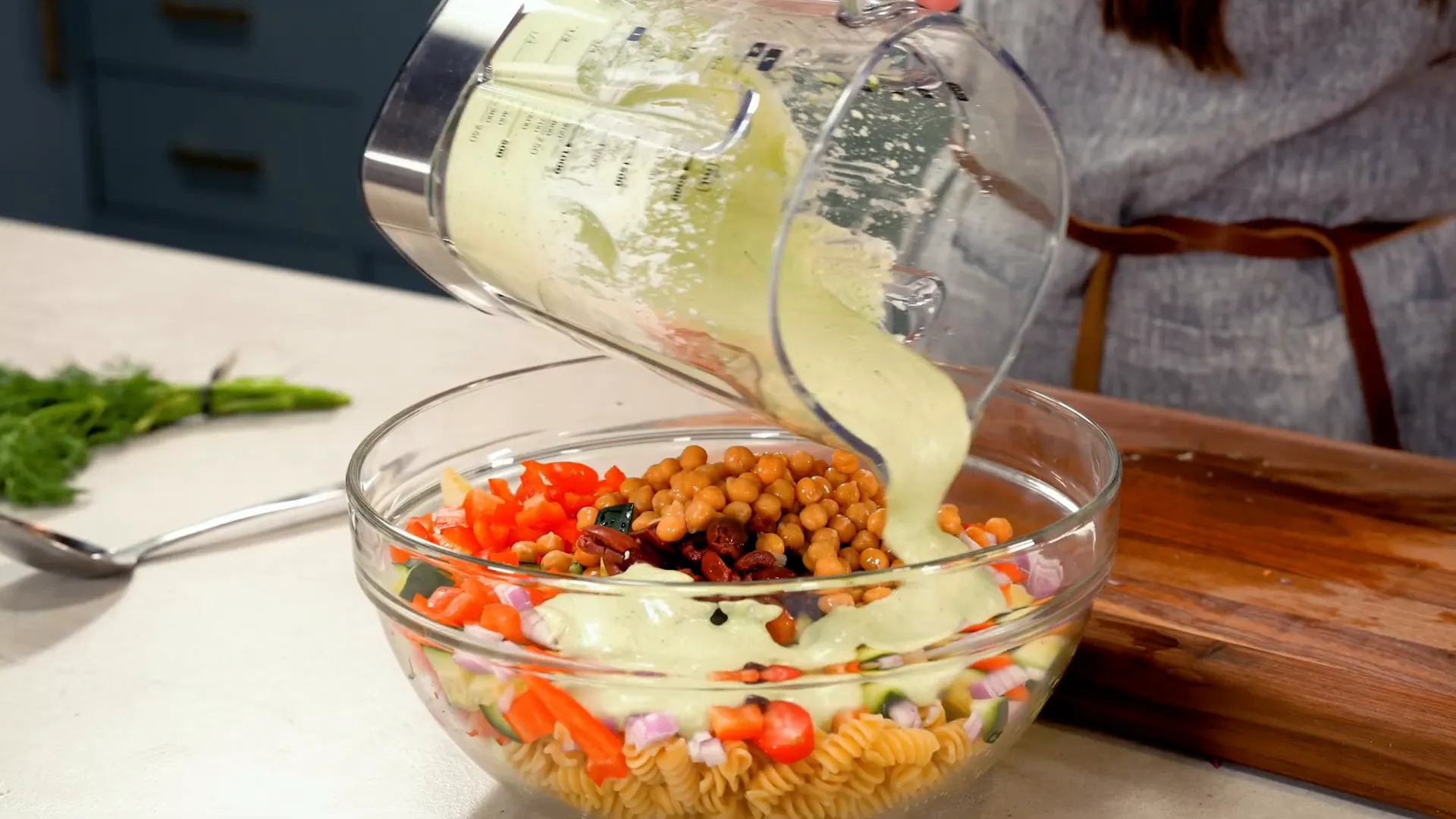 Mixing pasta, veggies, olives, chickpeas, and whipped feta dressing