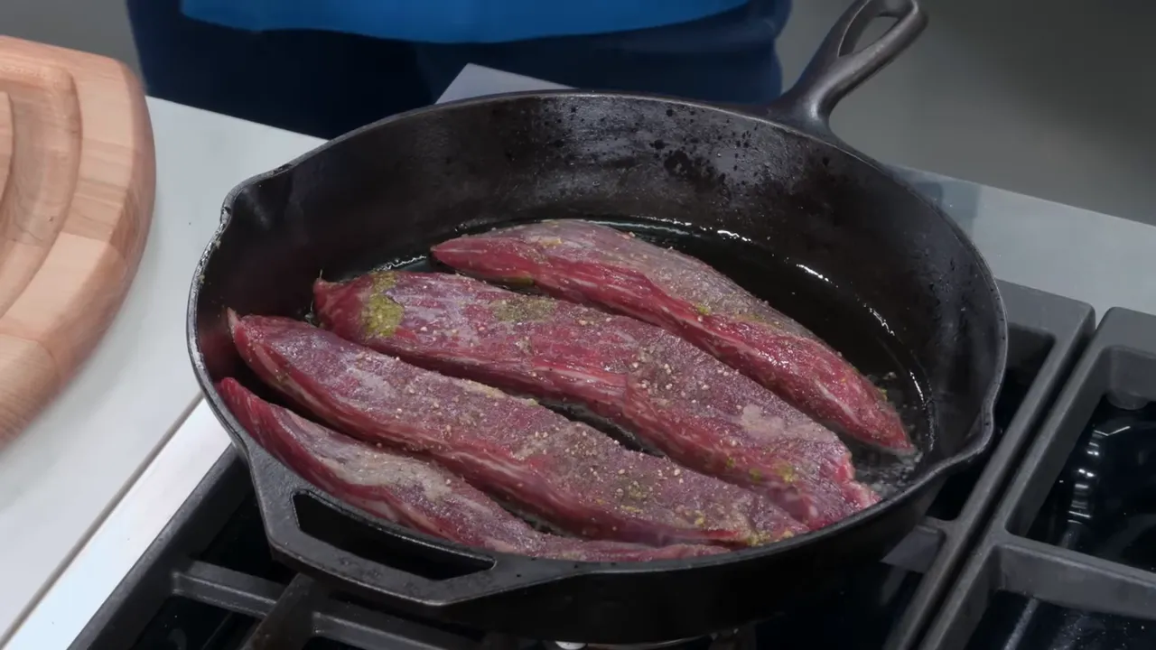 Searing long strips of flank steak in a very hot cast iron skillet